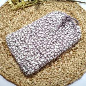 May include: A rectangular, hand-crocheted pouch in a basketweave pattern. The pouch is primarily lavender with white accents, and features a drawstring closure. The item is displayed on a woven, circular placemat.