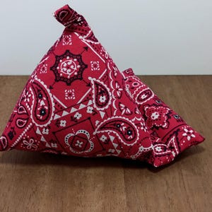 May include: Two red bandana-patterned fabric doorstops. The doorstops are triangular in shape and feature a classic paisley design in white and black against a red background. The doorstops are made of fabric and are designed to hold doors open.