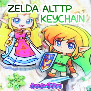 Peut inclure: Deux porte-clés en acrylique représentant des personnages de la série de jeux vidéo Zelda. L'un représente la princesse Zelda dans une robe rose et blanche, et l'autre Link avec une épée et un bouclier. Les porte-clés ont un fermoir doré et le texte "ZELDA ALTTTP KEYCHAIN".