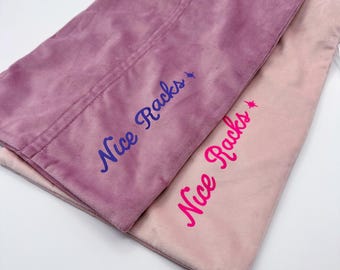 May include: Two rectangular velvet pillow covers in shades of mauve and light pink. The darker mauve cover features the text Nice Racks in dark purple, while the lighter pink cover displays the same text in bright pink, both with a small star.