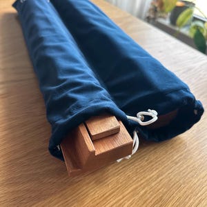 May include: Two navy blue velvet drawstring bags, each containing wooden components. The bags are partially open, revealing the light brown wood. The bags are on a light brown wooden surface. The bags are closed with a white drawstring.