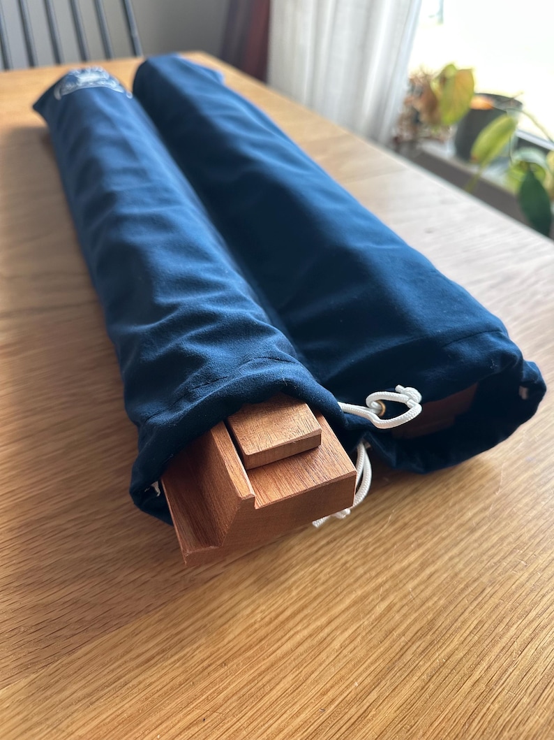 May include: Two navy blue velvet drawstring bags, each containing wooden components. The bags are partially open, revealing the light brown wood. The bags are on a light brown wooden surface. The bags are closed with a white drawstring.