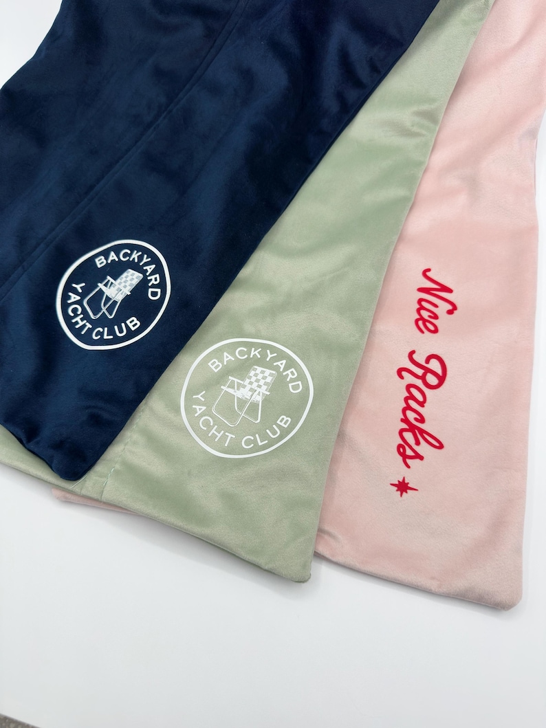 May include: Three velvet fabric items in navy blue, sage green, and pink. The navy blue and sage green items have a white embroidered "Backyard Yacht Club" logo. The pink item has red embroidered text that says "Nice Racks".