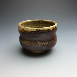 May include: A small, brown ceramic bowl with a white rim and a speckled glaze. The bowl has a rounded shape and a slightly flared lip.