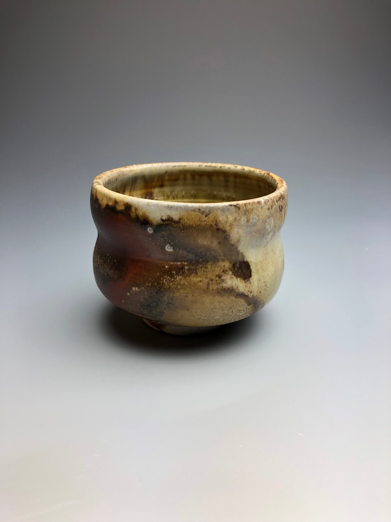 May include: A small, brown and white ceramic bowl with a slightly wavy rim. The bowl has a rustic, handmade look.