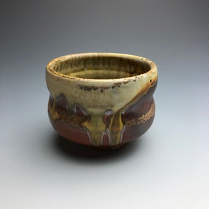 May include: A small, brown ceramic bowl with a textured, drippy glaze. The bowl has a rounded shape and a slightly flared rim.