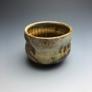 May include: A small, brown and white ceramic bowl with a textured, uneven surface. The bowl has a rounded shape and a slightly flared rim.