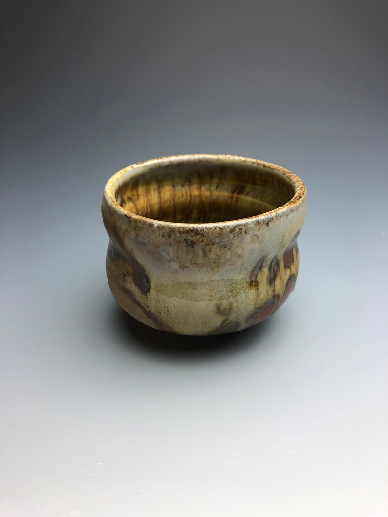 May include: A small, brown and white ceramic bowl with a textured, uneven surface. The bowl has a rounded shape and a slightly flared rim.