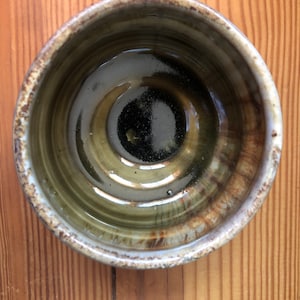 May include: A brown ceramic bowl with a white rim and a dark brown glaze inside. The bowl has a slightly textured surface and a glossy finish.
