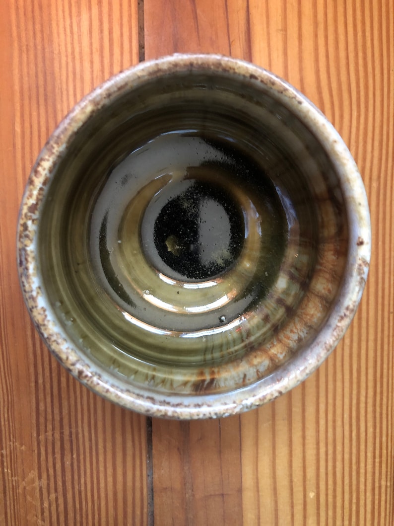 May include: A brown ceramic bowl with a white rim and a dark brown glaze inside. The bowl has a slightly textured surface and a glossy finish.