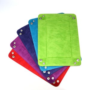 May include: A set of six colourful dice trays, each with a different colour: red, orange, purple, blue, teal, and green. The trays are made of a soft, suede-like material and have silver metal corners.