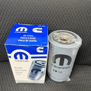 Puede incluir: Una caja de filtro de aceite MOPAR azul y blanca y un filtro de aceite gris. La caja tiene el logotipo de MOPAR y texto en ingl&eacute;s, franc&eacute;s y espa&ntilde;ol. El filtro de aceite tiene el logotipo de MOPAR y est&aacute; envuelto en pl&aacute;stico.