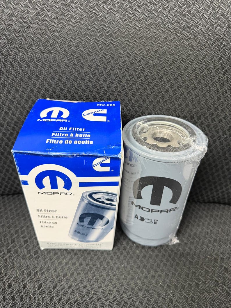 Puede incluir: Una caja de filtro de aceite MOPAR azul y blanca y un filtro de aceite gris. La caja tiene el logotipo de MOPAR y texto en ingl&eacute;s, franc&eacute;s y espa&ntilde;ol. El filtro de aceite tiene el logotipo de MOPAR y est&aacute; envuelto en pl&aacute;stico.