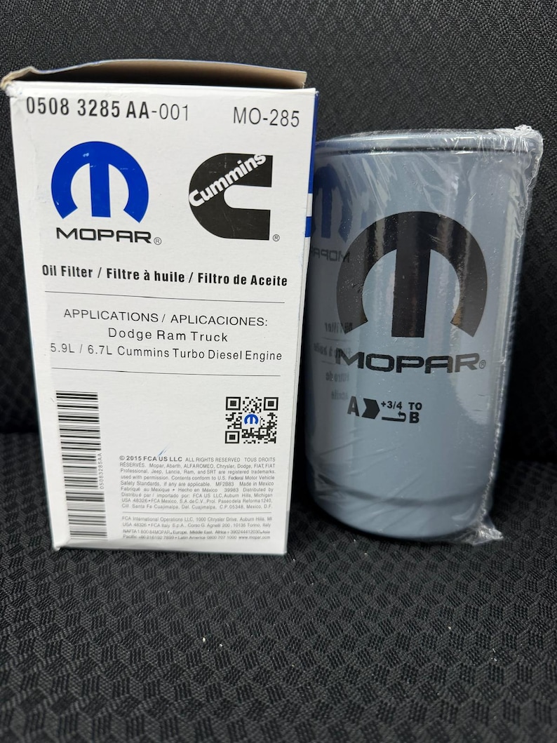 Puede incluir: Un filtro de aceite Mopar y su caja. La caja es blanca con texto azul y negro, incluyendo los logotipos de Mopar y Cummins. El filtro es gris con el logotipo de Mopar y est&aacute; envuelto en pl&aacute;stico transparente. La caja dice "Filtro de aceite" y "Dodge Ram Truck".