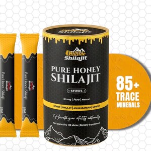 Op de afbeelding: Productafbeelding met een zwarte en gouden container van "Pure Honey Shilajit Sticks" en twee individuele stickverpakkingen. De container heeft een gele band en de tekst "85+ Trace Minerals". Het product is een voedingssupplement.