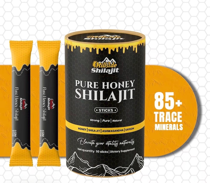 Op de afbeelding: Productafbeelding met een zwarte en gouden container van "Pure Honey Shilajit Sticks" en twee individuele stickverpakkingen. De container heeft een gele band en de tekst "85+ Trace Minerals". Het product is een voedingssupplement.