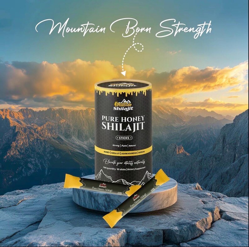 Op de afbeelding: Een productfoto van een zwart-gouden container met Hillside Shilajit Pure Honey Shilajit sticks. De container is cilindrisch en heeft bovenaan de tekst "Mountain Born Strength". Twee individuele honingsticks liggen voor de container. De achtergrond toont een bergketen.