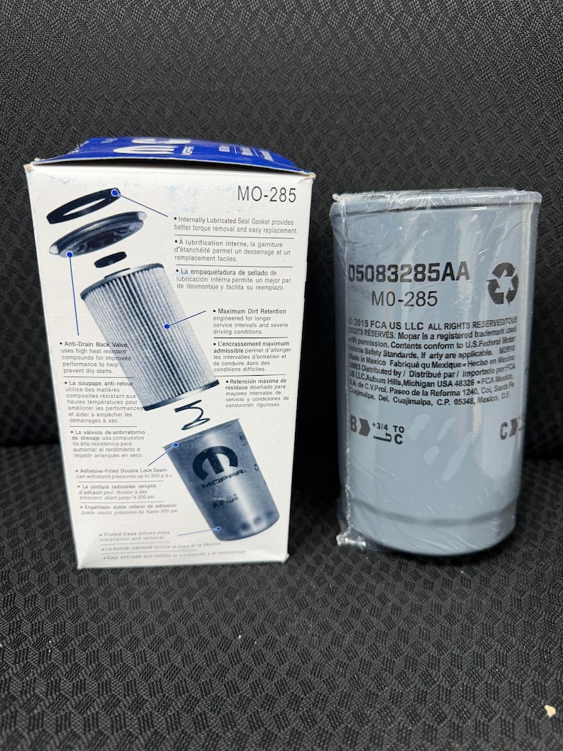 Puede incluir: Se muestran dos filtros de aceite automotrices, uno en caja y otro envuelto en pl&aacute;stico. La caja es blanca y azul, con texto y diagramas. El filtro envuelto es gris con texto impreso sobre un fondo oscuro.