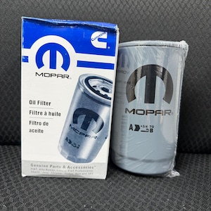 May include: A blue and white MOPAR oil filter box and a gray oil filter. The box has the MOPAR logo and text in English, French, and Spanish. The gray oil filter has the MOPAR logo and is wrapped in plastic.