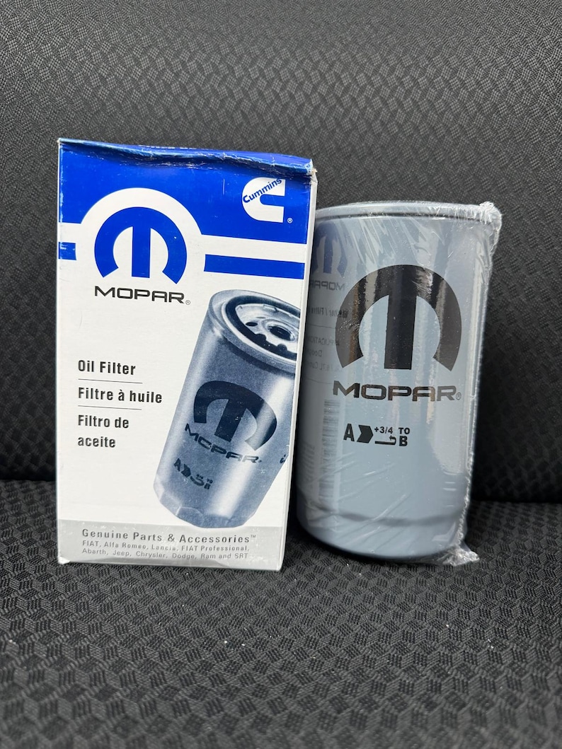 Puede incluir: Una caja de filtro de aceite MOPAR azul y blanco y un filtro de aceite gris. La caja tiene el logotipo de MOPAR y texto en ingl&eacute;s, franc&eacute;s y espa&ntilde;ol. El filtro de aceite gris tiene el logotipo de MOPAR y est&aacute; envuelto en pl&aacute;stico.