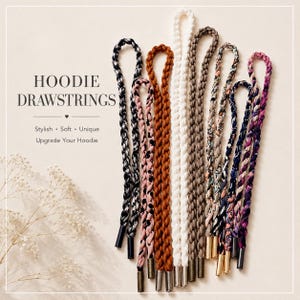 Peut inclure: Une collection de cordons de serrage tressés pour sweat à capuche dans diverses couleurs, notamment noir, blanc, marron, rose et des motifs. Chaque cordon présente des embouts métalliques. Le texte HOODIE DRAWSTRINGS, Stylish, Soft, Unique, Upgrade Your Hoodie est visible.