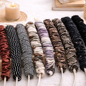 Puede incluir: Una colecci&oacute;n de organizadores de cables cubiertos de tela en varios colores y patrones. Los organizadores est&aacute;n dispuestos en una bandeja de madera, con dise&ntilde;os que incluyen burdeos liso, blanco y negro, y estampados de animales. Cada organizador est&aacute; unido a un cable blanco.