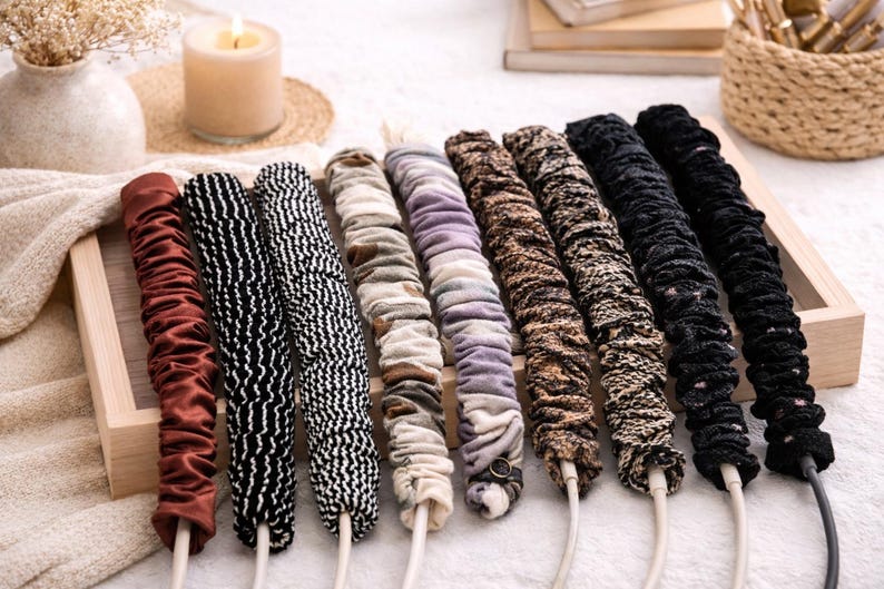 Puede incluir: Una colecci&oacute;n de organizadores de cables cubiertos de tela en varios colores y patrones. Los organizadores est&aacute;n dispuestos en una bandeja de madera, con dise&ntilde;os que incluyen burdeos liso, blanco y negro, y estampados de animales. Cada organizador est&aacute; unido a un cable blanco.