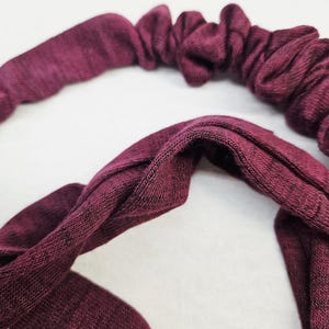 Puede incluir: Primer plano de una diadema burdeos con tejido de punto texturizado. La diadema presenta una secci&oacute;n fruncida y el&aacute;stica y una banda m&aacute;s ancha y lisa. El tejido tiene un sutil efecto jaspeado, que a&ntilde;ade profundidad al color.
