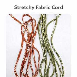 May include: Two lengths of stretchy fabric cord. One is a rust color with white floral patterns, and the other is olive green with white floral patterns. The text "Stretchy Fabric Cord" is at the top of the image.