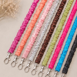 May include: A collection of ten scrunchie-style fabric straps in various colors including magenta, orange, light pink, silver, brown, lime green, hot pink, blue, and black, each featuring a silver-toned metal lobster clasp at the end.