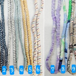 Op de afbeelding: Tien lange, met stof beklede elastische koorden, verticaal gerangschikt en genummerd van &eacute;&eacute;n tot tien. De koorden hebben verschillende patronen en kleuren, waaronder bruin, blauw, grijs, lichtblauw, geel, gestreept, paars, groen, bloemen en beige.