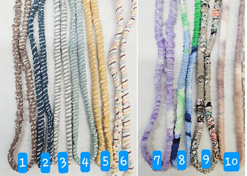 Op de afbeelding: Tien lange, met stof beklede elastische koorden, verticaal gerangschikt en genummerd van &eacute;&eacute;n tot tien. De koorden hebben verschillende patronen en kleuren, waaronder bruin, blauw, grijs, lichtblauw, geel, gestreept, paars, groen, bloemen en beige.