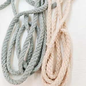May include: Two spools of thick, braided rope. One spool is a light gray color and the other is a light beige color.
