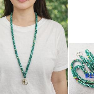 K&ouml;nnte beinhalten: Ein Stoff-Lanyard mit einer blaugr&uuml;nen Grundfarbe und einem mehrfarbigen Blumenmuster mit wei&szlig;en, gelben und rosa Akzenten. Das Lanyard verf&uuml;gt &uuml;ber einen goldfarbenen Karabinerhaken und einen Schl&uuml;sselring. Die Nummer 15 ist blau aufgedruckt.