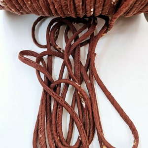 May include: A close-up of brown cord with a subtle floral pattern. The cord is twisted and looped, showing its texture and flexibility.