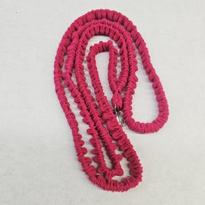 May include: A long, bright magenta leash featuring a gathered, ruffled fabric texture throughout its length. The leash includes a silver-toned metal swivel clasp at one end, designed for secure attachment, and is coiled into a series of loops.