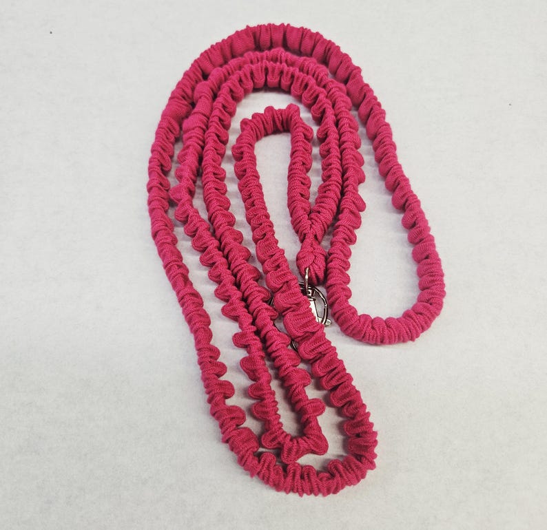 May include: A long, bright magenta leash featuring a gathered, ruffled fabric texture throughout its length. The leash includes a silver-toned metal swivel clasp at one end, designed for secure attachment, and is coiled into a series of loops.