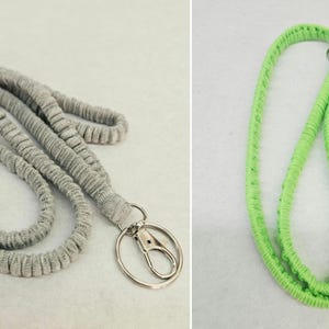May include: A grey fabric lanyard with a silver-toned metal lobster clasp and a split ring, alongside a bright lime green fabric lanyard. Both lanyards feature a textured, ribbed surface design and are constructed from a soft, flexible material.