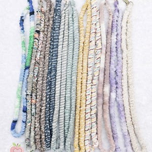 Puede incluir: Una colección de cordones coloridos con varios patrones y texturas. Cada cordón presenta un diseño diferente, incluyendo colores florales, a rayas y lisos, y está terminado con un cierre metálico. Los cordones se muestran sobre un fondo blanco.