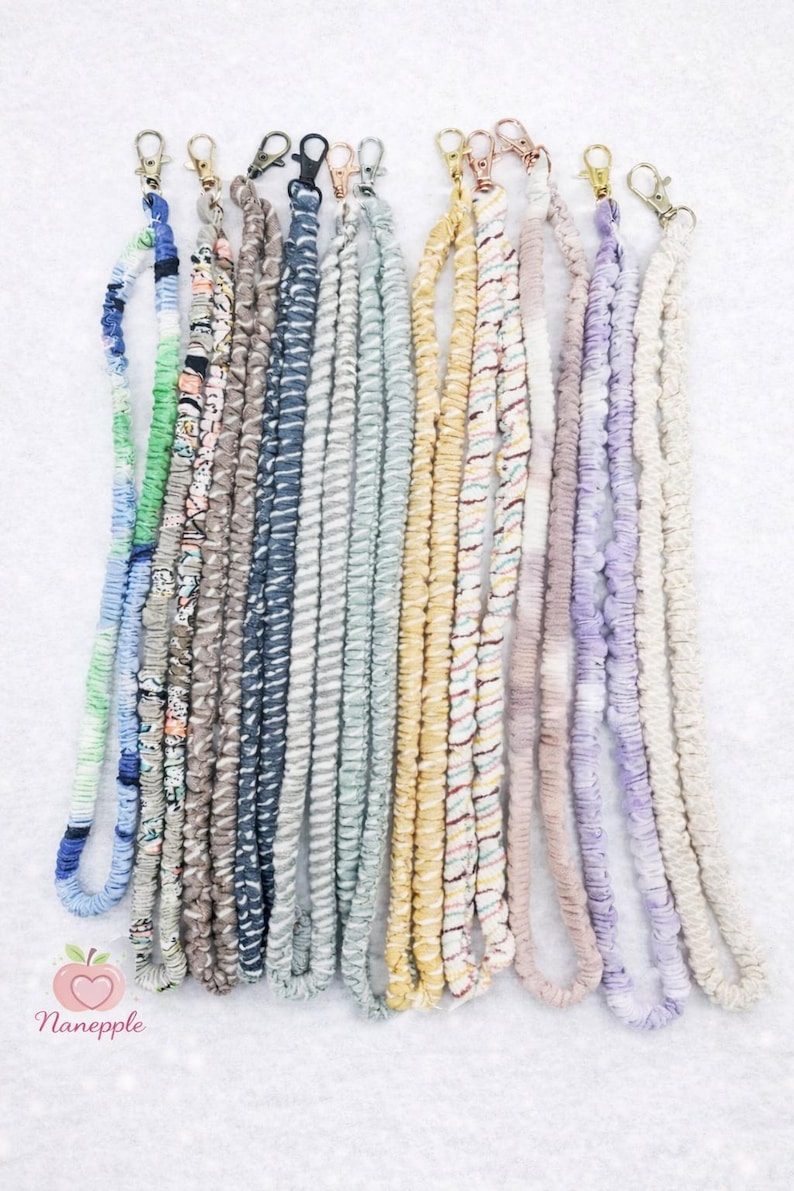 Op de afbeelding: Een collectie van twaalf stoffen keycords in diverse kleuren en patronen, waaronder blauw, groen, geel, paars en neutrale tinten. Elk keycord heeft een geplooide scrunchie-textuur en is afgewerkt met een metalen karabijnhaak.