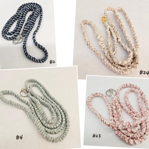 Op de afbeelding: Vier lanyards met metalen sluitingen, gelabeld #2, #4, #23 en #24. De lanyards hebben een gewikkeld, met stof bekleed ontwerp in marineblauw met wit, lichtgrijs, oudroze en beige, elk met een zilver- of goudkleurige metalen draaibare haak.