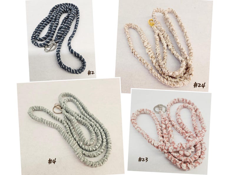 Op de afbeelding: Vier lanyards met metalen sluitingen, gelabeld #2, #4, #23 en #24. De lanyards hebben een gewikkeld, met stof bekleed ontwerp in marineblauw met wit, lichtgrijs, oudroze en beige, elk met een zilver- of goudkleurige metalen draaibare haak.