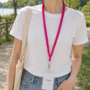 May include: A bright fuchsia lanyard featuring a textured, corded fabric design with a silver-toned metal swivel lobster clasp. Attached to the clasp is a clear plastic vertical badge holder containing a white card with the printed text ID CARD.