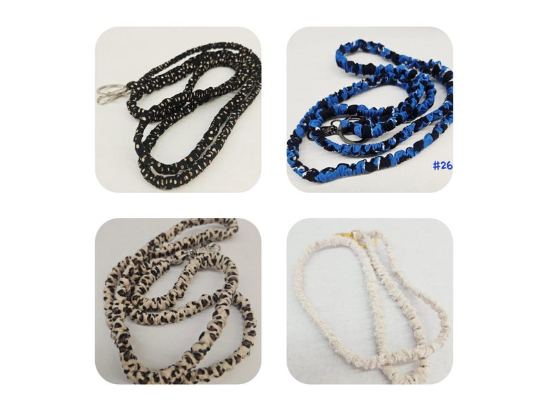 K&ouml;nnte beinhalten: Vier Stoff-Lanyards mit Metallverschl&uuml;ssen. Eines ist schwarz mit wei&szlig;en Punkten, eines ist blau-schwarz gemustert mit dem Text #26, eines ist beige mit braunem Leopardenmuster und eines ist einfarbig cremewei&szlig;. Jedes Lanyard hat ein gerafftes Stoffdesign.