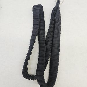 May include: A black fabric lanyard featuring a gathered, elasticized texture throughout the length of the strap. The lanyard is finished with a circular silver-toned metal split ring attachment at the top for securing keys or identification badges.