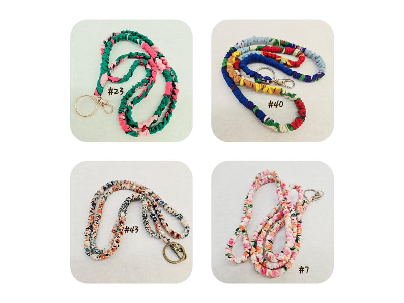 K&ouml;nnte beinhalten: Vier Stoff-Lanyards mit Metall-Schl&uuml;sselringen und Karabinerverschl&uuml;ssen. Nummer 23 ist gr&uuml;n und pink, Nummer 40 ist mehrfarbig, Nummer 43 zeigt ein kleines Blumenmuster und Nummer 7 weist einen pink-wei&szlig;en Blumendruck auf dem Stoff auf.