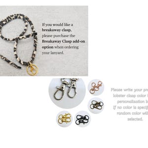 May include: A black and white patterned fabric lanyard with a gold-toned lobster clasp. The image includes text regarding a breakaway clasp add-on and displays various lobster clasp color options in silver, rose gold, bronze, gold, and black.