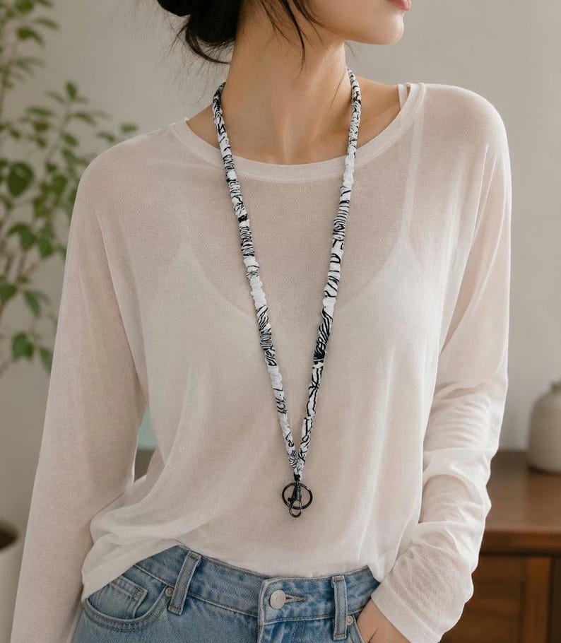 K&ouml;nnte beinhalten: Ein Stoff-Lanyard mit einem schwarz-wei&szlig;en, abstrakten Marmormuster. Das lange, schmale Band besteht aus gerafftem Material und verf&uuml;gt &uuml;ber einen schwarzen, runden Metallring sowie einen kleinen Karabinerverschluss am unteren Ende.