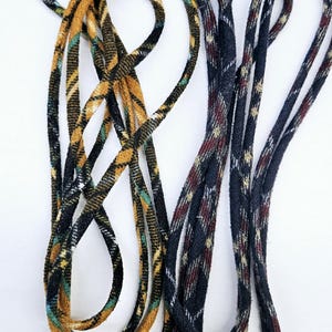 May include: A close-up of three different patterned shoelaces. The shoelaces are made of a woven fabric and have a variety of colors, including black, brown, white, and green.