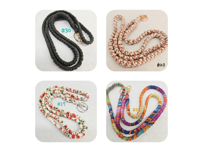 Op de afbeelding: Vier stoffen lanyards met metalen sluitingen. Nummer 30 is effen zwart. Nummer 20 is een bruin en wit patroonkoord. Nummer 17 heeft een witte stof met een rode en groene bloemenprint. Nummer 25 is een meerkleurig koord met diverse tinten.